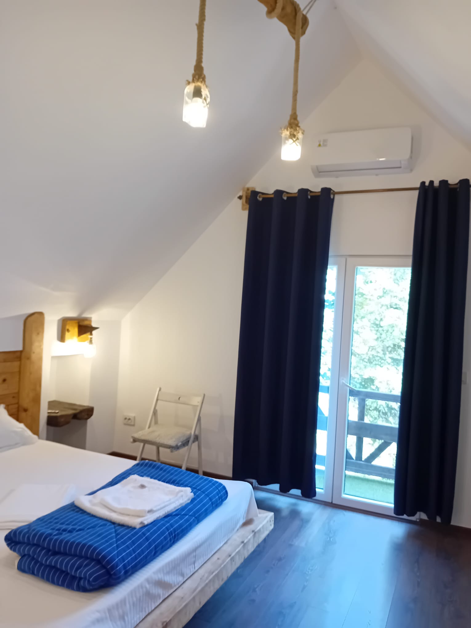 Attic room with rope pendant lights and balcony door showing garden trees at Magic Garden